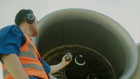 Musician Jordan Rakei in a safety vest and headphones records the sound of a jet engine.