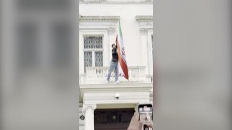 A protester is on the balcony of the Iranian embassy, tearing down a flag