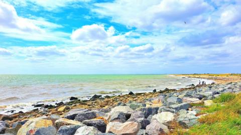 A brightly coloured rocky beach below a partially cloudy sky