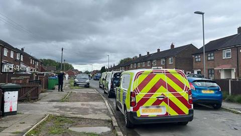 Police vehicles lined up on residential street - Rowrah Crescent in Middleton - on a cloudy day. 