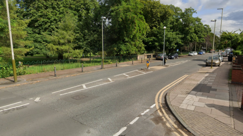An urban road next to a park with trees in it 