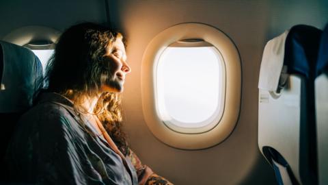 Serene female passenger enjoying sunny view from airplane window - stock photo