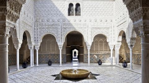 A courtyard with tiled floor, fountain and white ornately carved walls