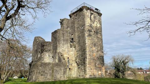 The ruins of an old castle, on top of a hill with part of Glasgow spreading behind it