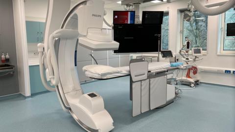 A modern hospital imaging room with a large Philips C‑arm scanner positioned over a patient bed, surrounded by monitors and medical equipment.