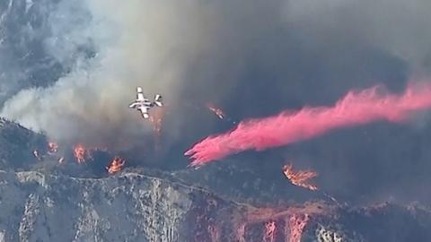 A fire fighting aeroplane drops fire retardant on a burning hillside.