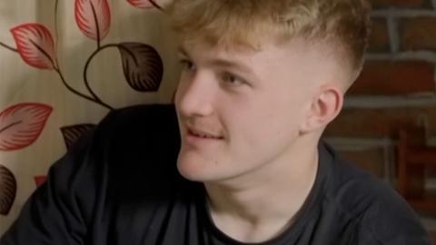 Fin, wearing a black T-shirt and sitting in a hostel room