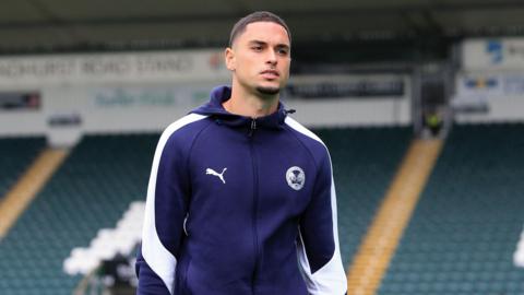 Klaidi Lolos, dressed in a navy blue Peterborough United training top with white trim on the shoulders and sleeves