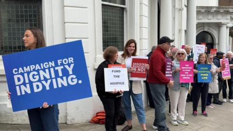 Campaigners with placards for and against the Assisted Dying Bill gather outside the Isle of Man's white parliament building.