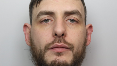 Mugshot of Ashley Pointon in a grey t shirt. He has brown hair and a brown beard.