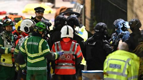 Police officers stand with British Transport Police officers and emergency officials outside Huntingdon Station in England