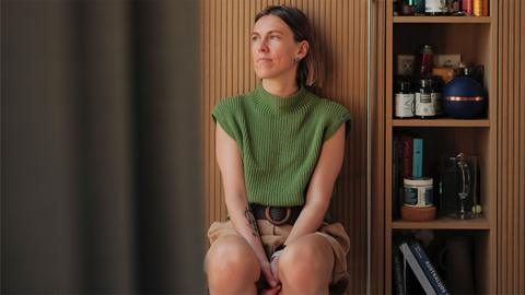 Milda Mitkutė, founder of Vinted is sat at home wearing a green top and light brown shorts. 