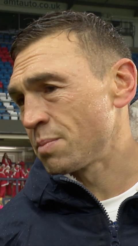 Kevin Sinfield looks off camera in a blue coat, soaking with rain on his face.