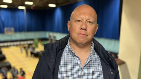 A bald man with a dark blue coat and a checkered shirt.