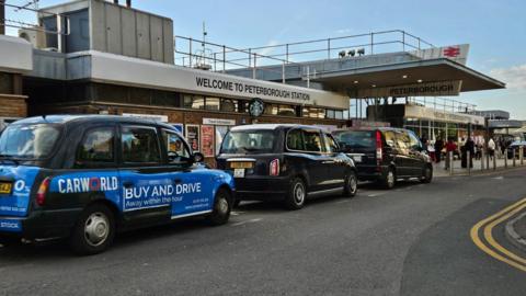 A row of black cabs parked outside Peterborough railway station.