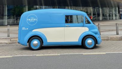 A retro looking blue and cream van with blue wheel trims is parked outside the Wales Millennium Centre. A logo on the side of the vehicles says 'The Travel Show'.