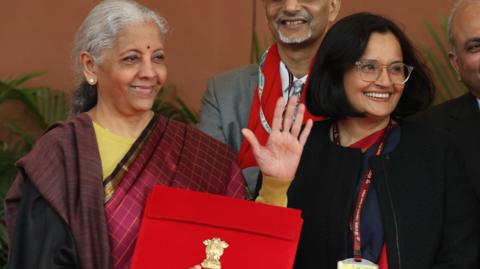 India's Finance Minister Nirmala Sitharaman (R) leaves the Finance Ministry office to present the annual budget to the parliament wearing a traditional Indian saree and carrying a red briefcase with the budget documents. She is surrounded by government officials. Photo by RAJAT GUPTA/EPA/Shutterstock
