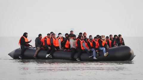 A black dinghy full of people wearing orange life jackets in the sea near Gravelines, France, on Saturday.
