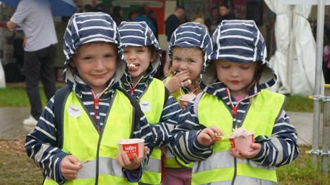 Pedwar o blant bach mewn siacedi hi-vis yn bwyta hufen ia o botiau