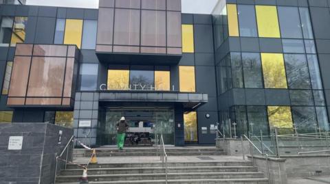 A modern-looking council building.  There are steps leading to the entrance which has sliding doors.  A person is leaving the building and walking towards the camera.