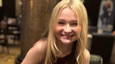Isla, who has long blonde hair, smiles at the camera.