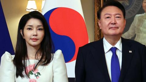 South Korean President Yoon Suk Yeol and his wife, Kim Keon Hee stand in front of a South Korean flag