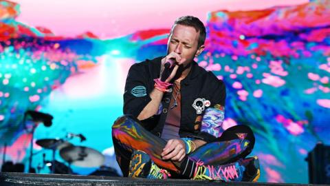 chris martin sitting on stage during radio 1 big weekend set