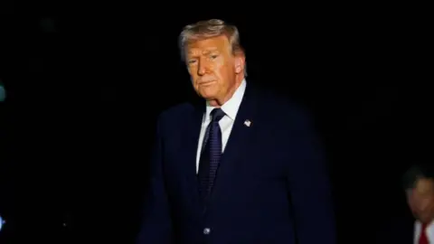 Donald Trump looks at the camera wearing a dark suit.