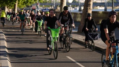 Several peeople riding bikes along the River Thames 