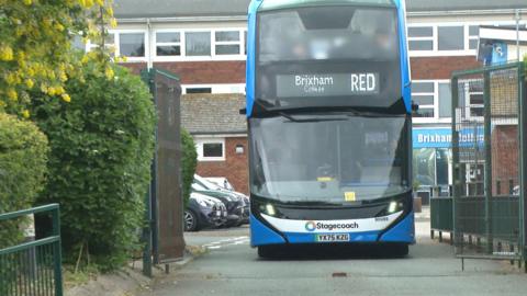 A blue double-decker bus with the Stagecoach logo on the front passes through the gates of a college car park.