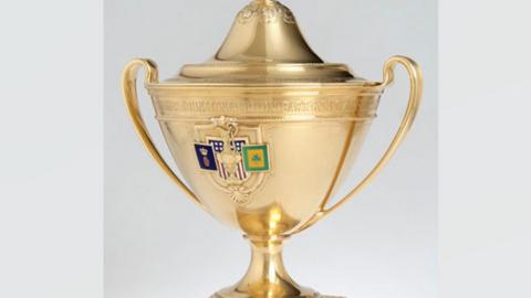 Gold trophy with dome lid and handles. A crest has badges on it 