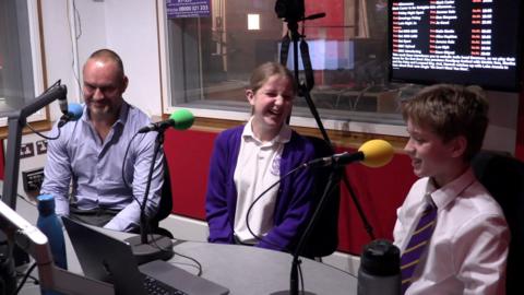 Mr Spooner sits in the Radio Oxford studio with students Emily and James