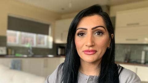 Sharanjeet in a grey jacket, sat in a kitchen