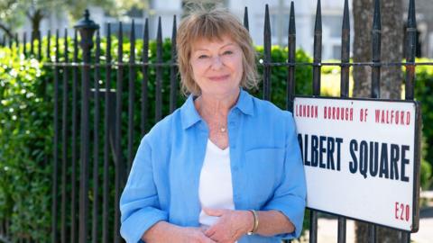 Karen Henthorn smiling next to an 'Albert Square' sign