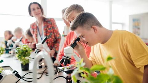 GCSE students in a biology class looking into microscopes with plant samples on desk.