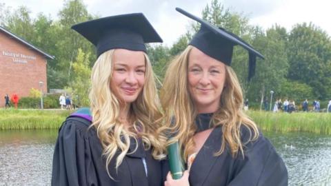 Mia Kennedy, left, with her mum, right, both in graduation gowns and hats, smiling with long hair.