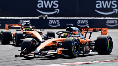 The McLaren of Lando Norris is pushed into position by his mechanics on the grid before the start of the Hugarian Grand Prix