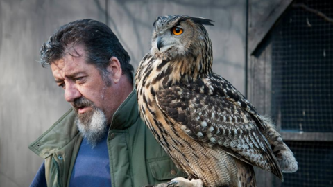 Mike Gibb, left, with green jacket and blue top, beside an Owl with amber and black eyes