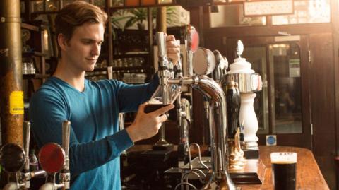 A man wearing a blue top pouring a pint in a pub