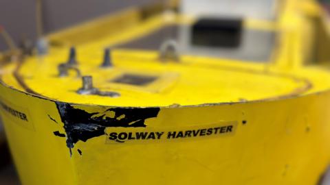 A closeup of the bow of a model of the Solway Harvester, which is painted bright yellow but has paint chipped off the front. Its nameplate is clearly visible with Solway Harvester in black lettering.