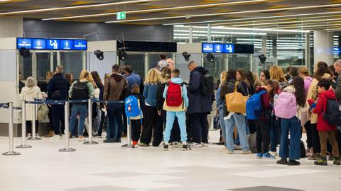 Travellers with luggage queue at arrivals as officials in booths marked "all passports" check passports at Split Airport in Croatia.