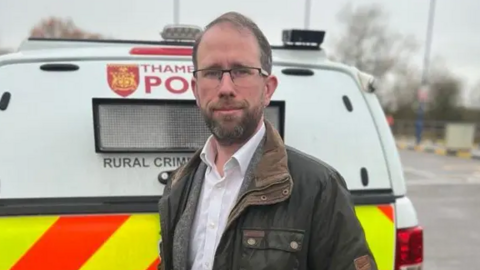 Matthew Barber, dressed in a coat, stood at the back of a Thames Valley Police van.