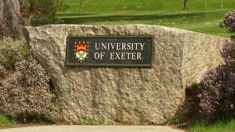 A sign reading University of Exeter issued against a stone wall