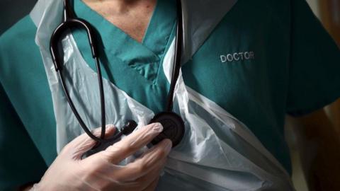 A doctor in green scrubs holding a stethoscope.