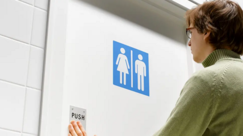 Person walking into a toilet with a unisex gender sign on the door