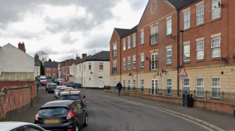 A Google Streetview image of Surrey Street. It has a three storey residential building to the right of the road and a row of parked cars on the left.