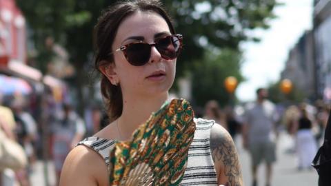 Woman in stripy top and sunglasses carrying a fan