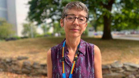 Chief medical officer Vanessa Purday has short grey hair. She is wearing a purple top with a rainbow lanyard.