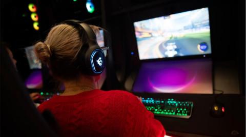 A woman wearing a gaming headset looks at a screen set up in the new e-sports facility.