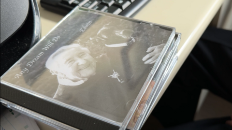 A CD with the photo of a man and his dog. It is black and white and is resting on a white table on top of other CD's. 